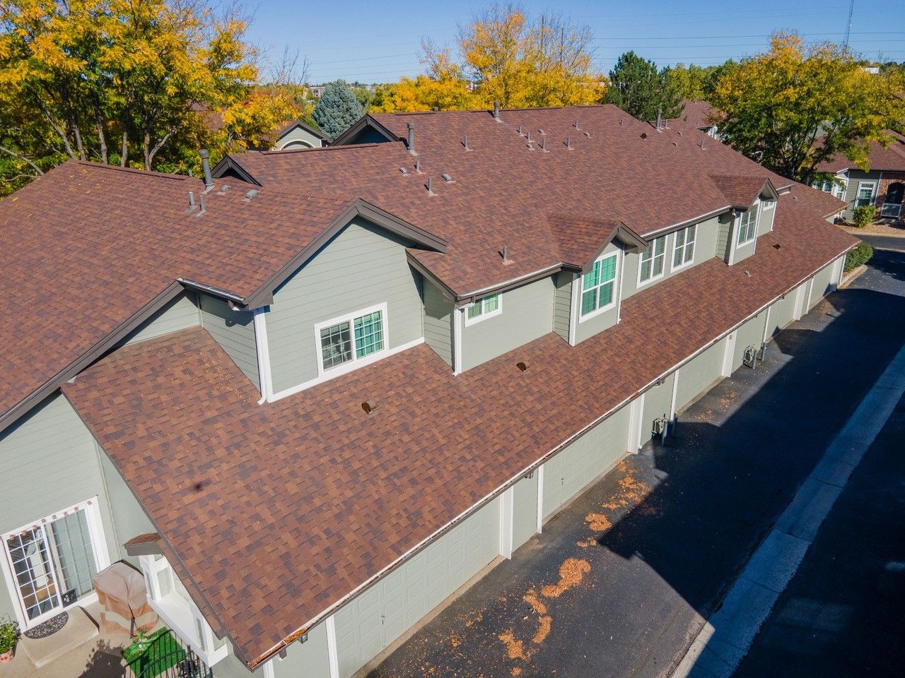 Aerial view of a red-roofed apartment building with a parking lot and autumn trees nearby