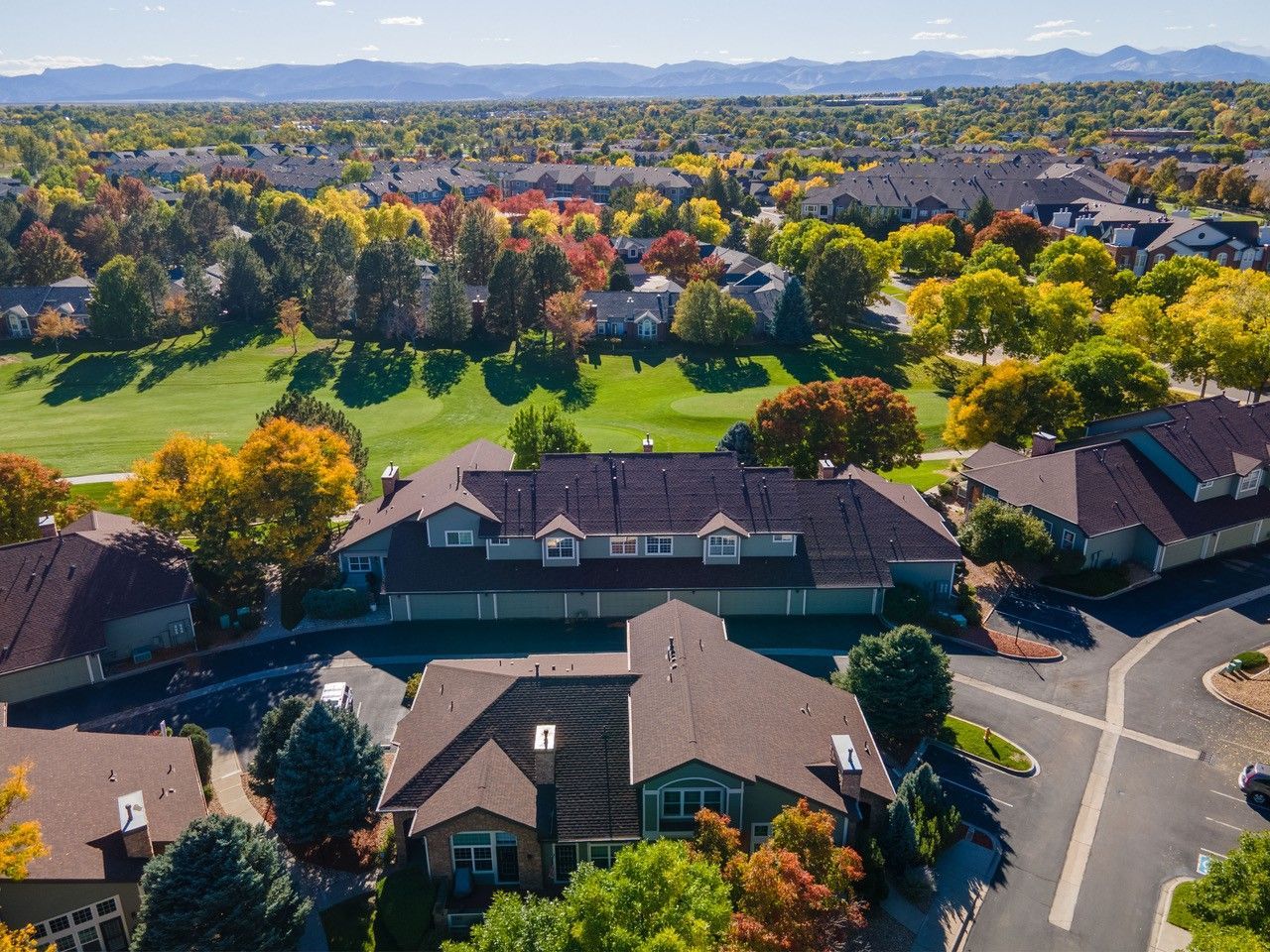 Aerial view of suburban homes beside a green park with autumn trees and distant mountains.