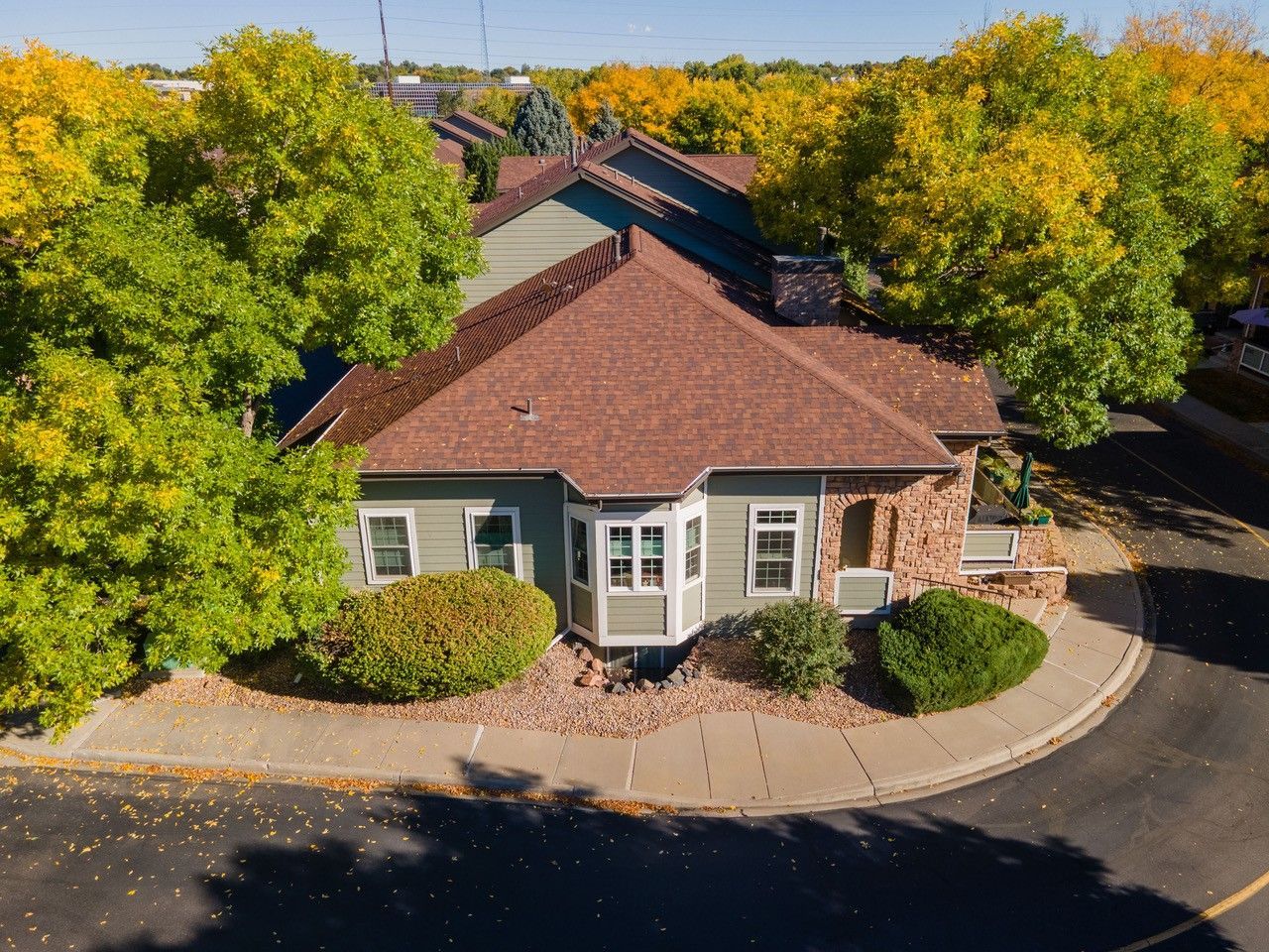 Aerial view of a small brick building with a dark roof, surrounded by trees and shrubs in autumn.