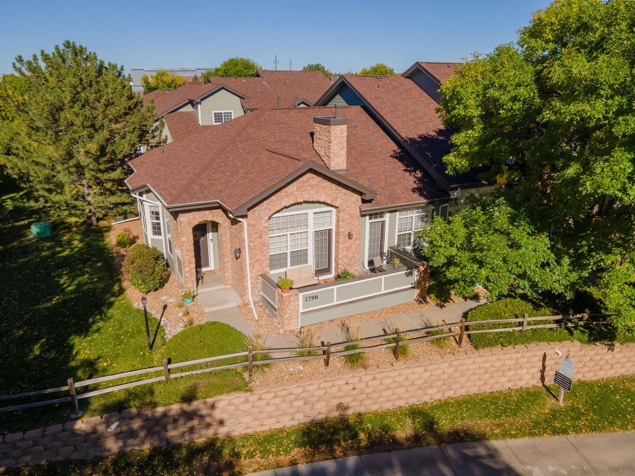 Brick house with red roof beside a tree-lined path on a sunny day.