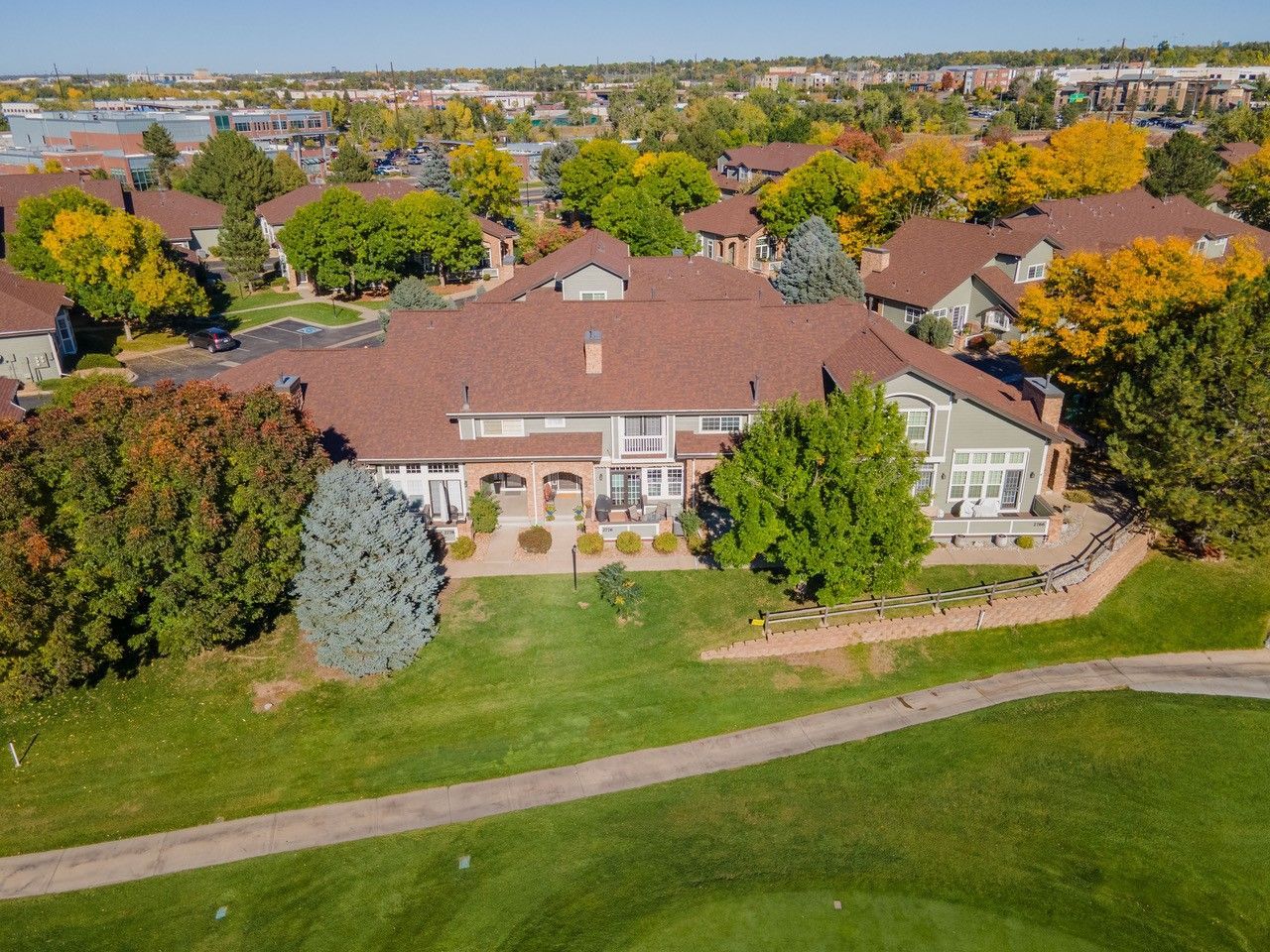 Aerial view of a large tan house with a red roof, surrounded by green trees and lawn.
