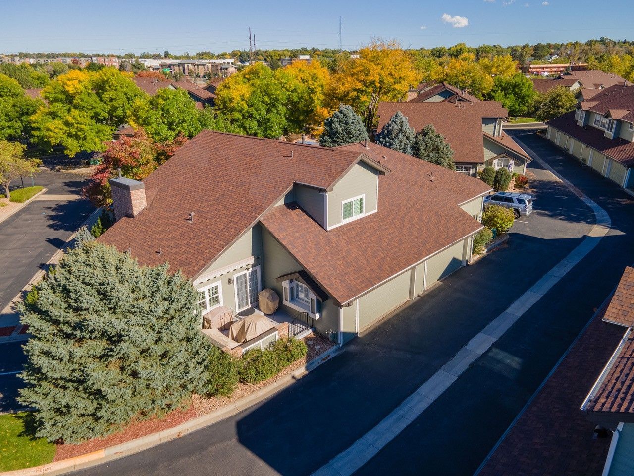 Aerial view of a suburban house with a red roof, trees, and nearby streets in autumn.