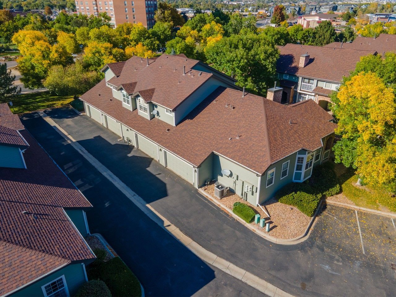 Aerial view of a tan building with a brown roof, surrounded by trees and a paved parking lot.