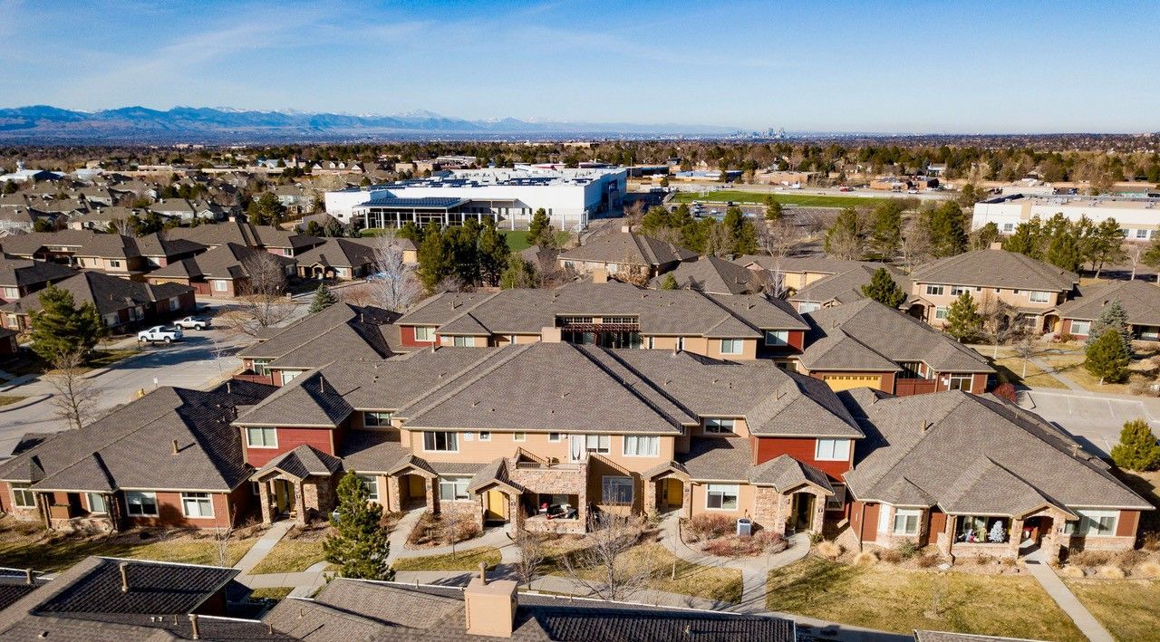Aerial view of a large suburban apartment complex with gray roofs and a swimming pool in the background.