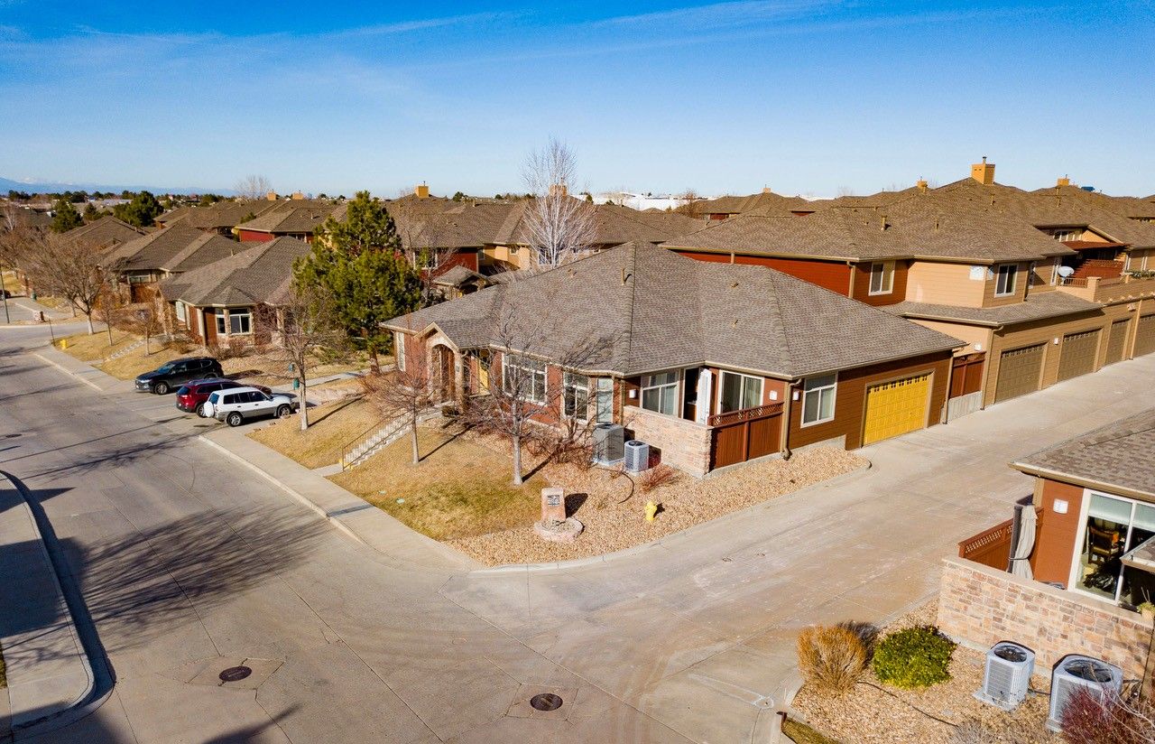 Aerial view of a suburban neighborhood with brick houses, driveways, and parked cars under a clear blue sky.