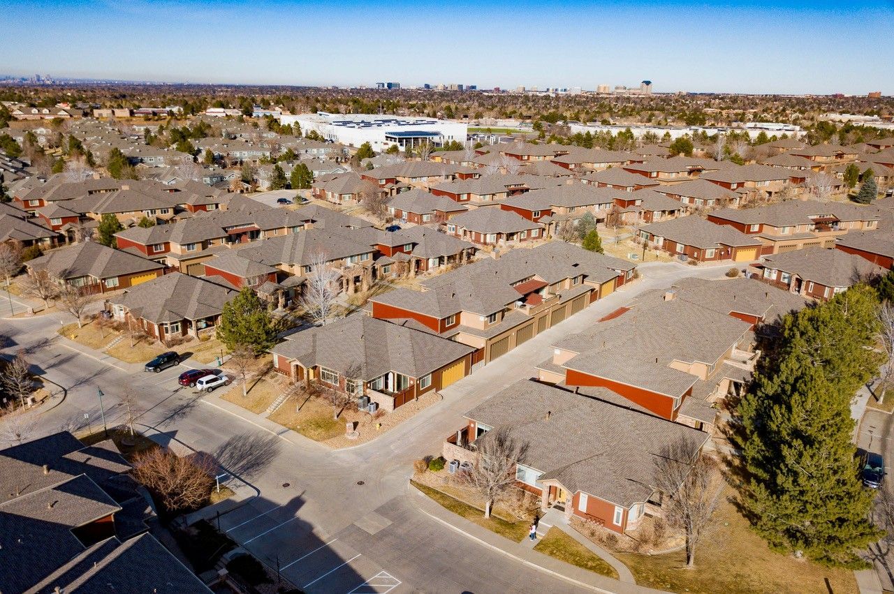 Aerial view of a suburban apartment complex with tan roofs and tree-lined streets under a clear sky.