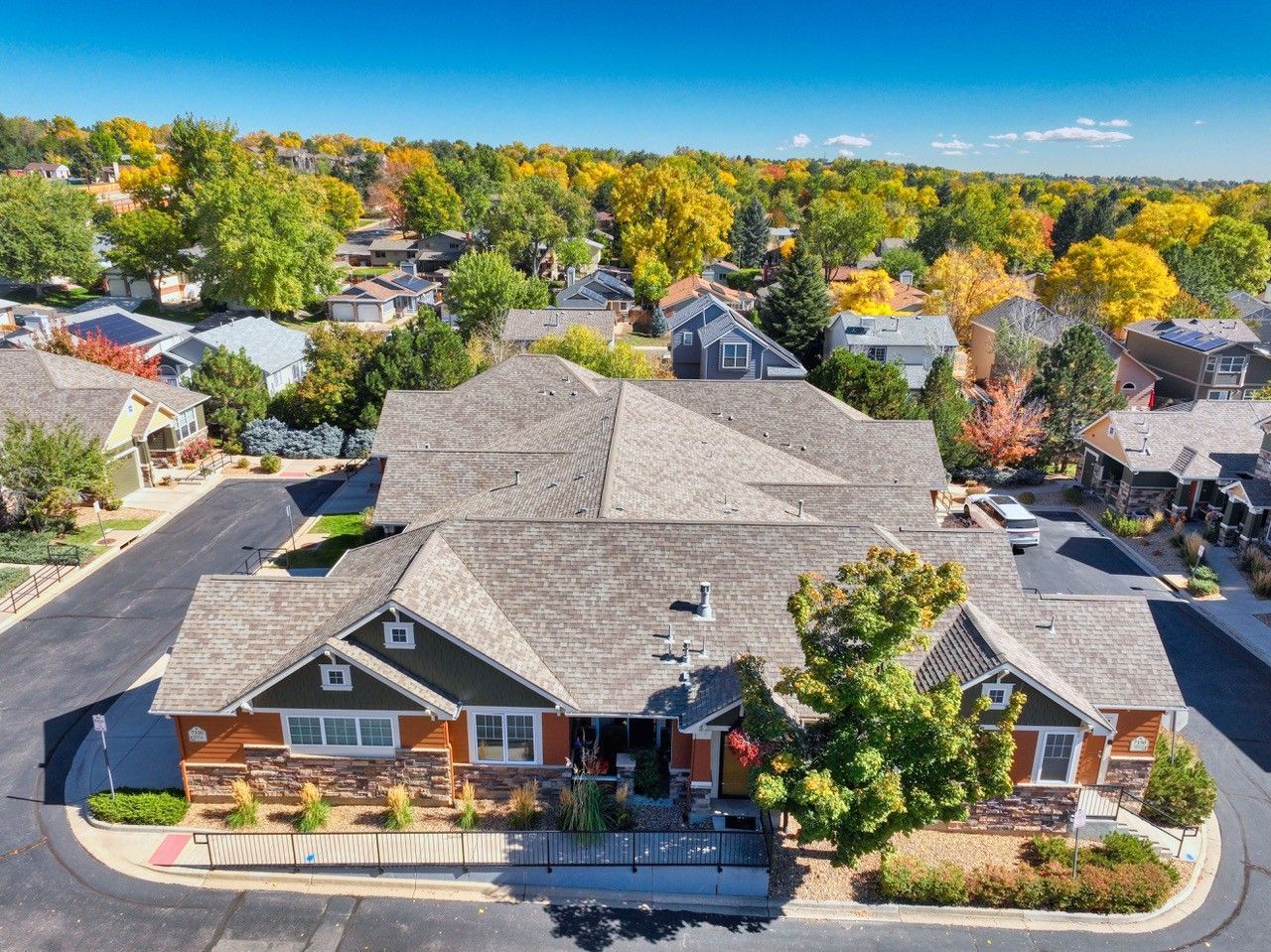 Aerial view of a large brick building with gray roofs, surrounded by homes and autumn trees.