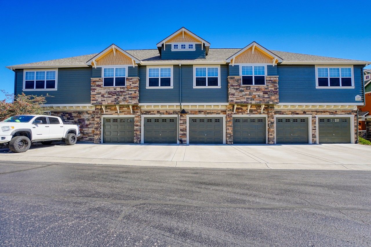 Stone-and-blue apartment building with five garage doors and a white SUV in front.