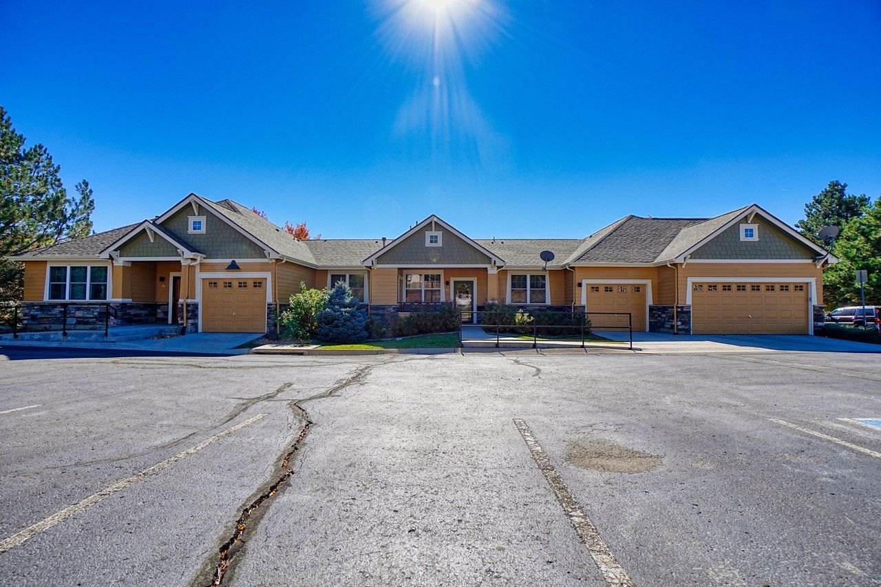Single-story apartment buildings with garages under a bright blue sky, viewed from a large cracked parking lot.