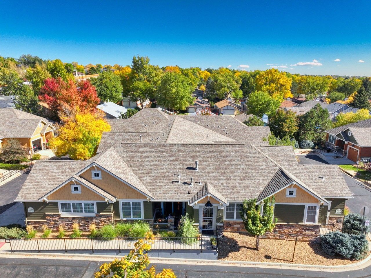 Aerial view of a suburban house with a gray roof, surrounded by colorful autumn trees.