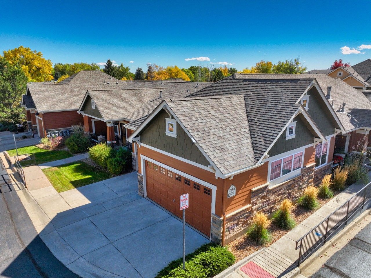 Aerial view of suburban townhouse rooftops and garage, with trees and a street below.