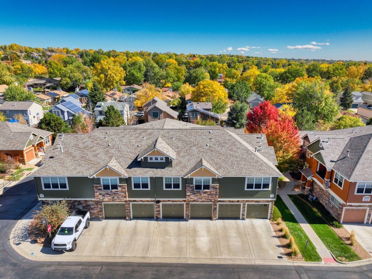 Aerial view of a row of townhouses with autumn trees and suburban homes in the background.