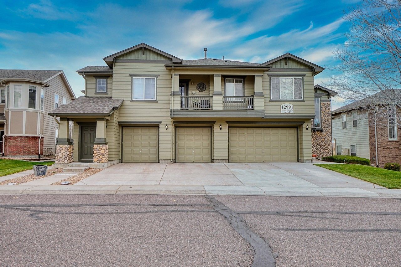 Two-story beige suburban house with a three-car garage and a wide driveway.