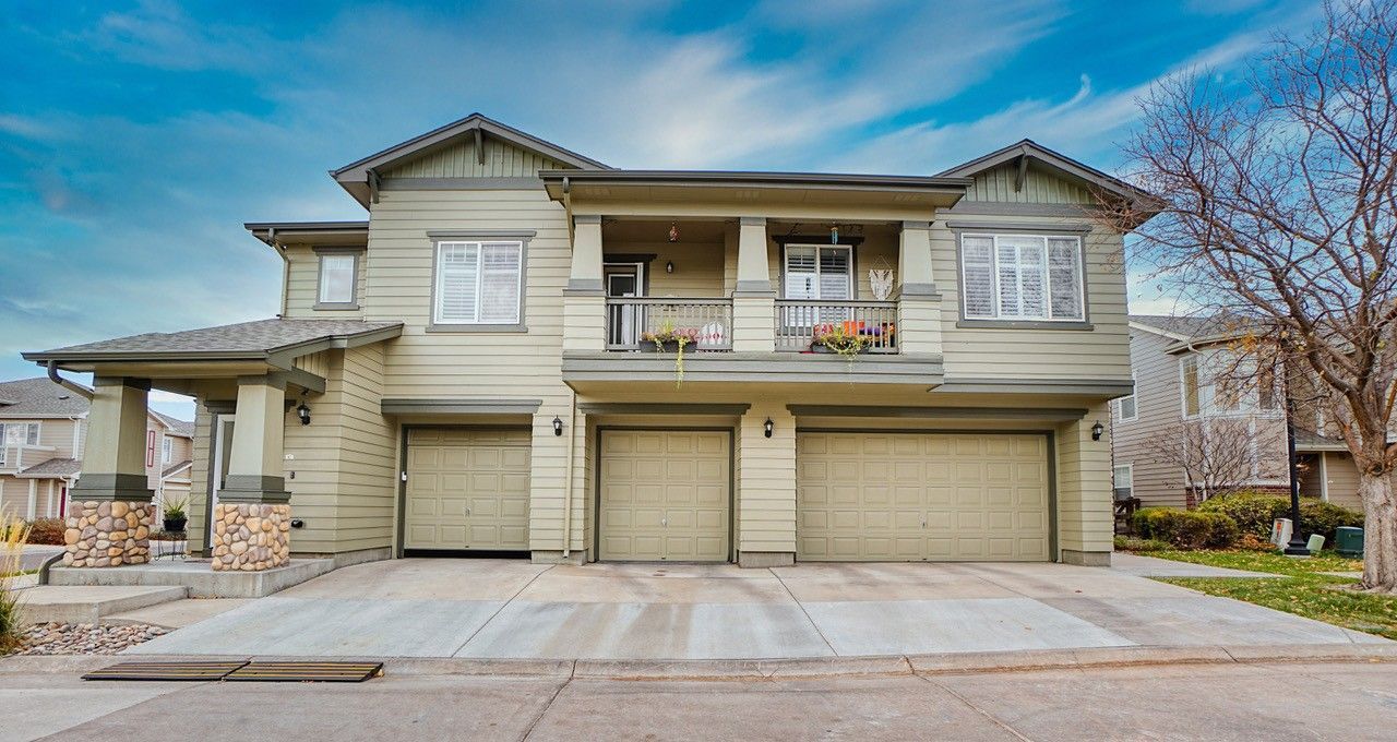 Two-story beige suburban house with three garages and a small balcony under a blue sky.