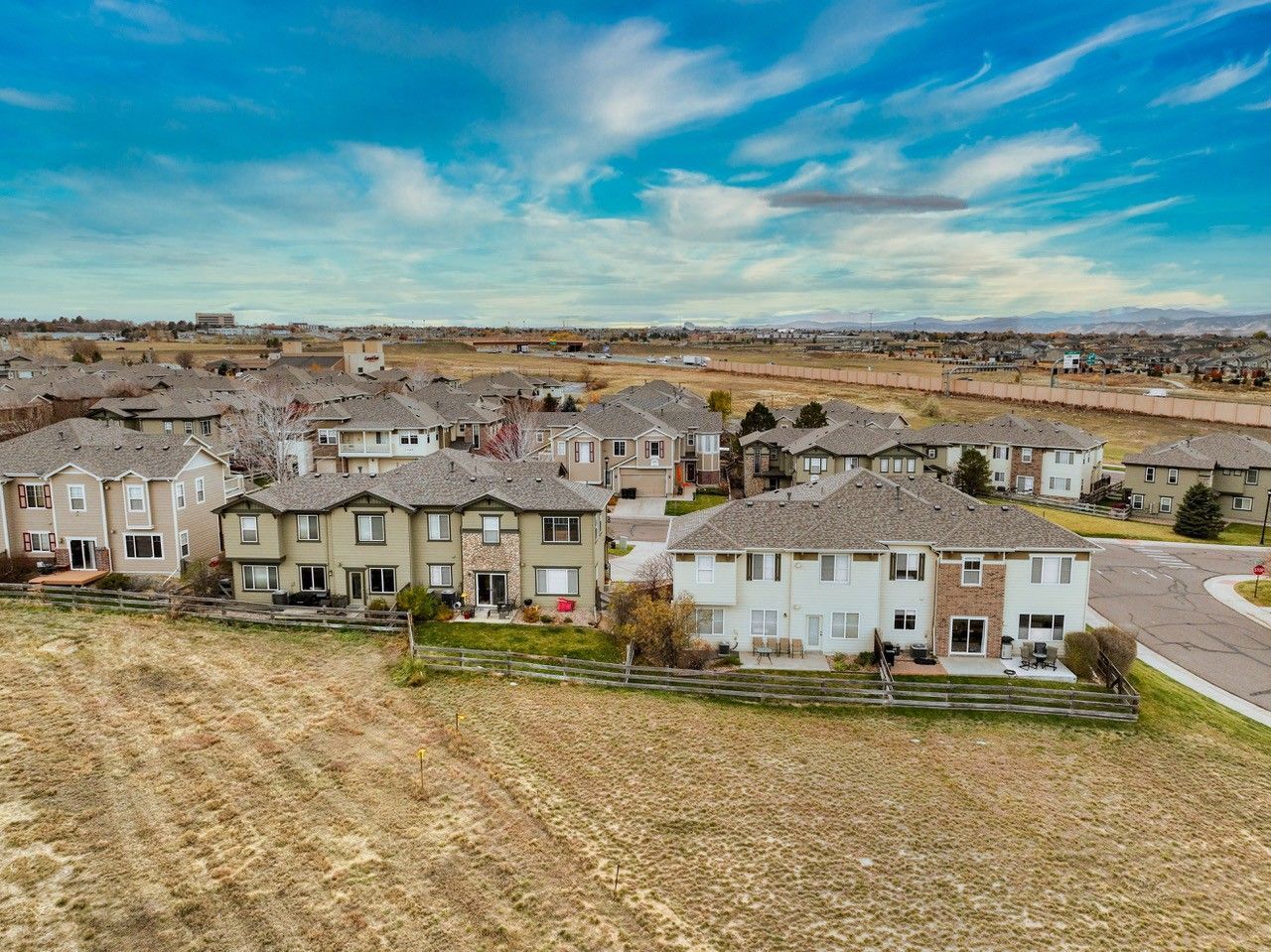 Suburban neighborhood with rows of houses, dry grass, and a cloudy blue sky.