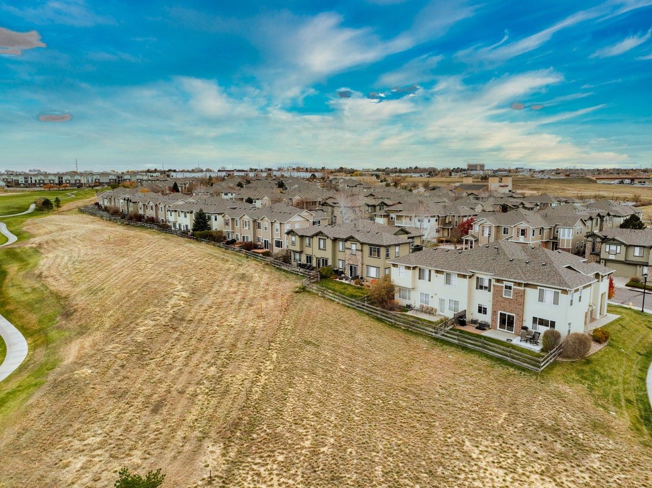 Aerial view of a suburban housing estate beside a large grassy field under a blue sky.