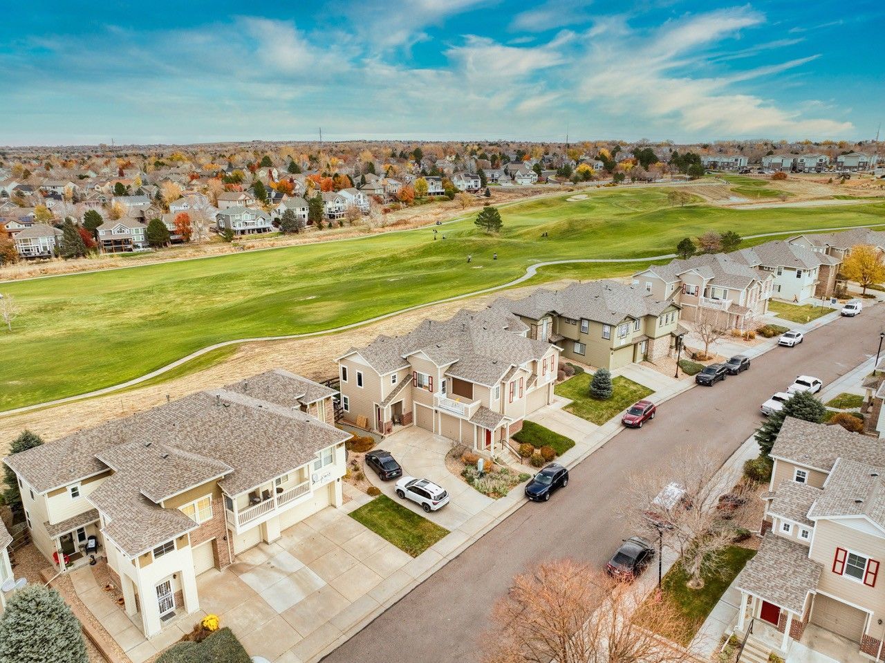 Aerial view of a suburban neighborhood beside a green field under a clear blue sky.