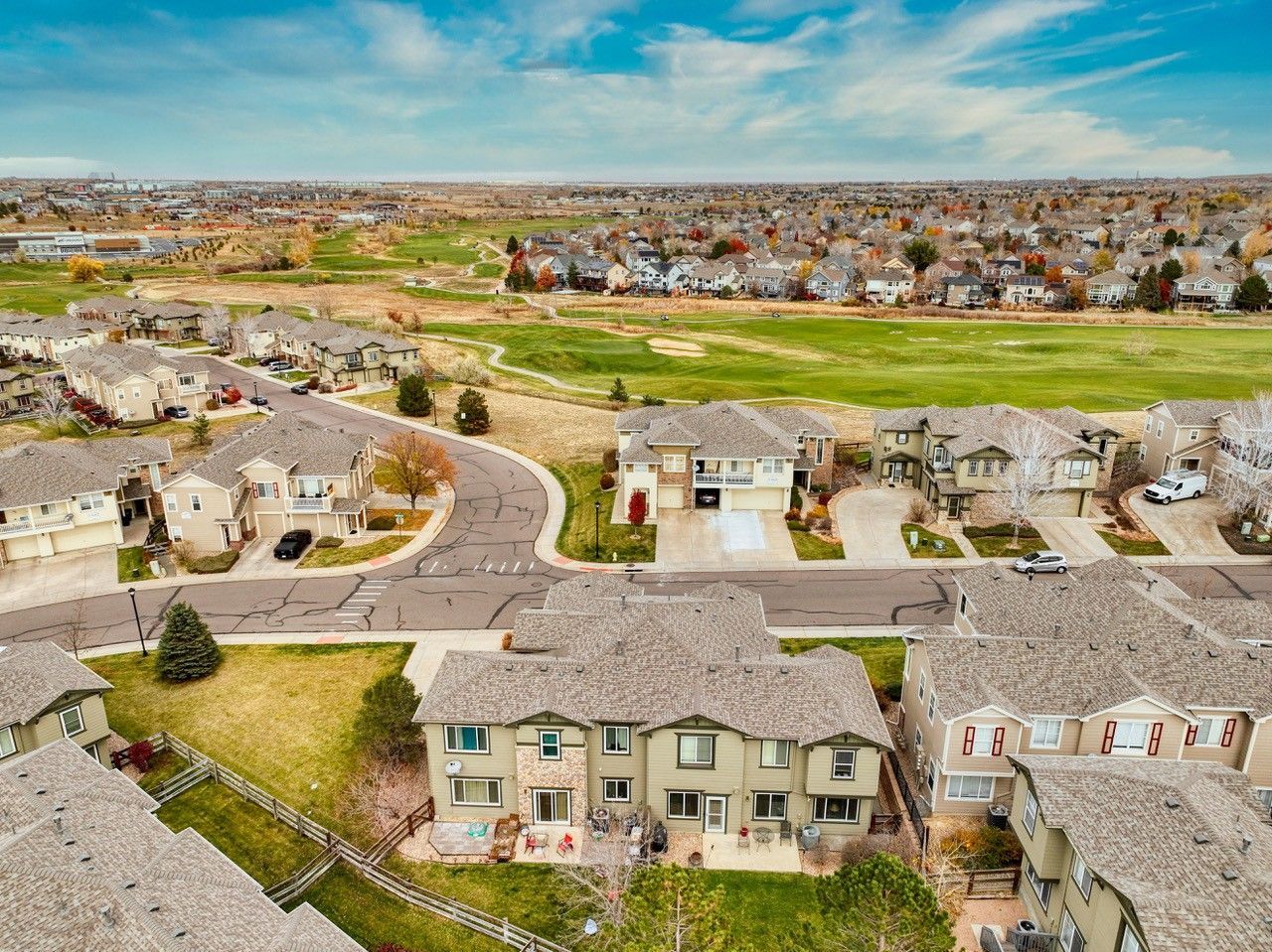 Aerial view of a suburban neighborhood with homes, curved streets, and green open fields beyond.