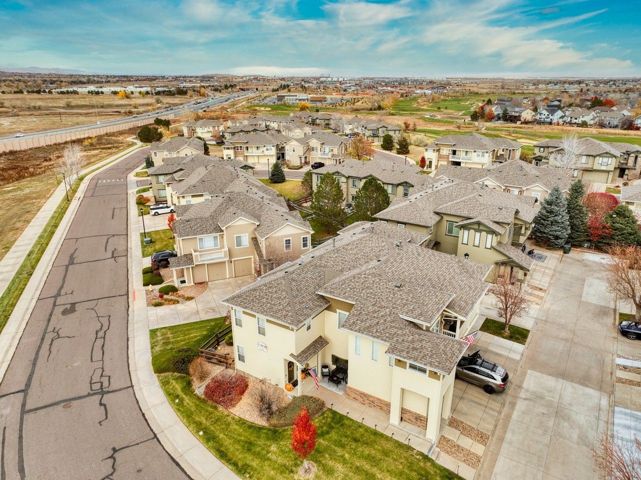 Aerial view of a suburban neighborhood with beige houses, tiled roofs, and a road under a blue sky.