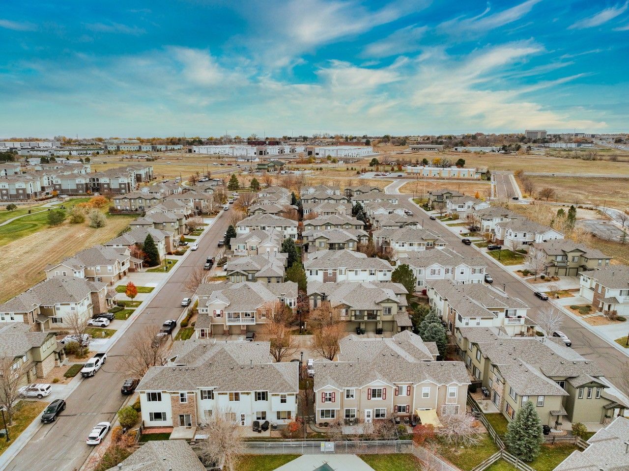 Aerial view of a suburban neighborhood with rows of houses and streets under a partly cloudy sky.