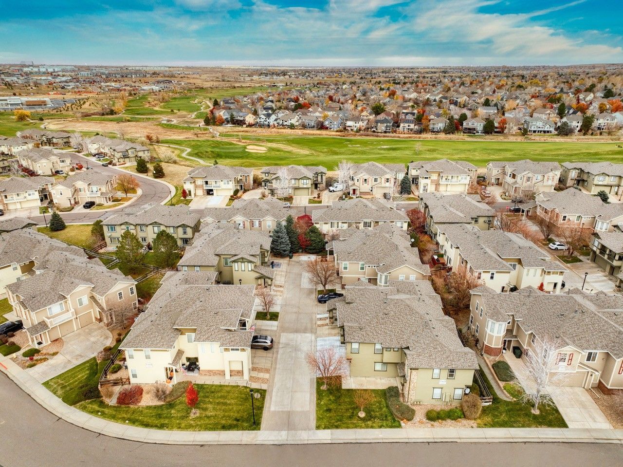Aerial view of a suburban neighborhood with rows of beige houses under a blue sky.