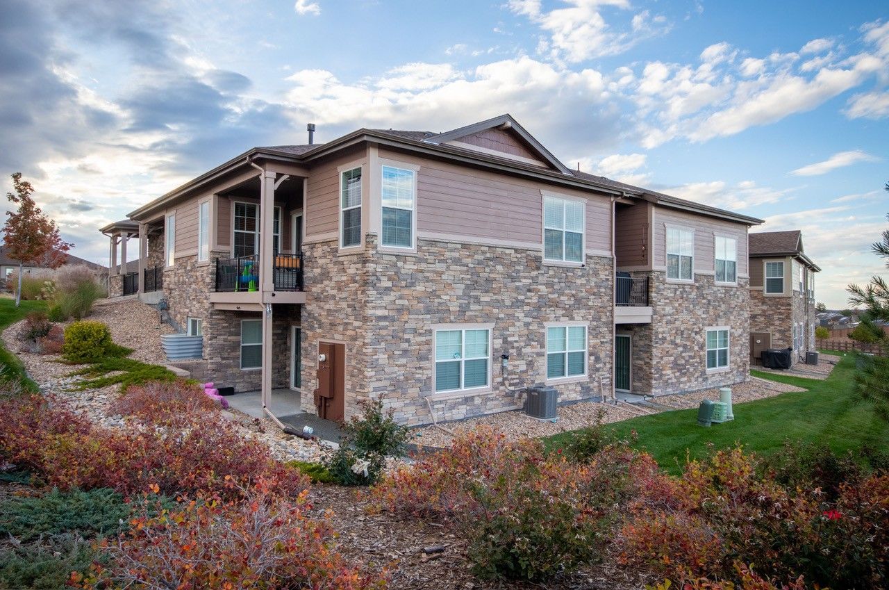Apartment building with stone and beige siding, surrounded by desert landscaping under a cloudy sky.