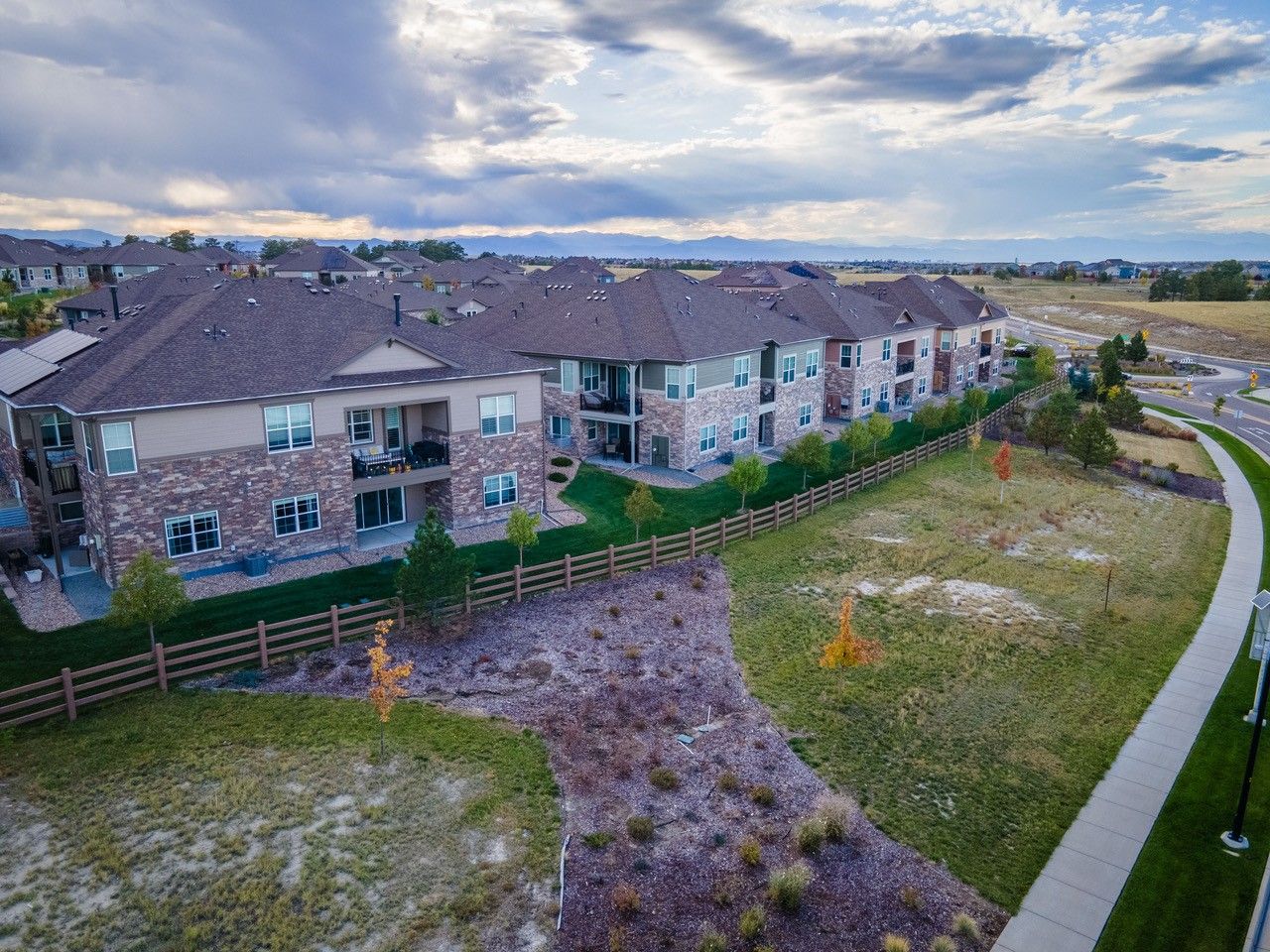 Apartment buildings beside a grassy path and fenced courtyard under a cloudy sky.