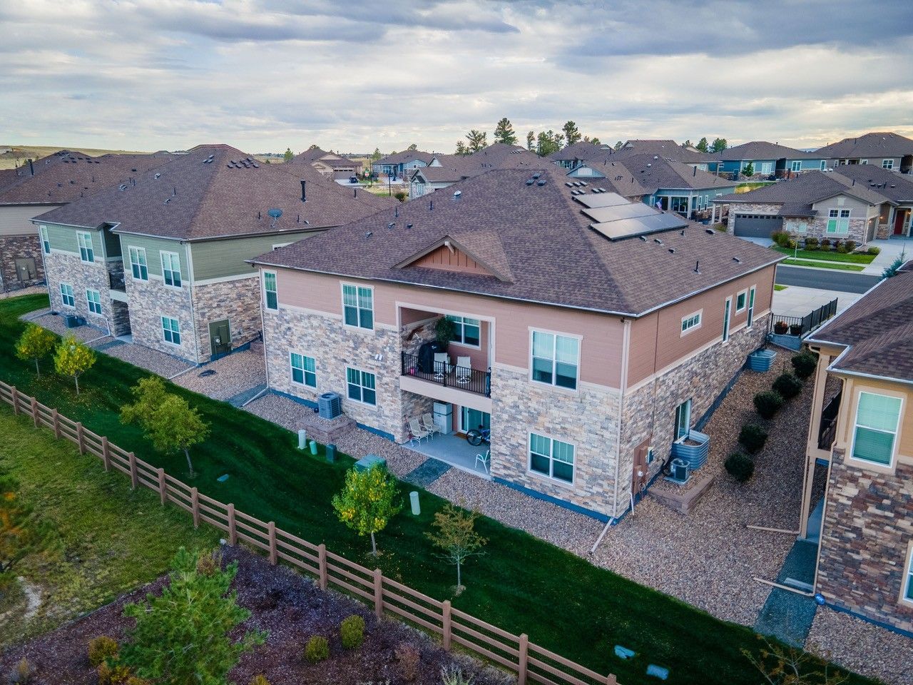 Aerial view of beige townhouses with brown roofs and fenced backyards in a suburban neighborhood.