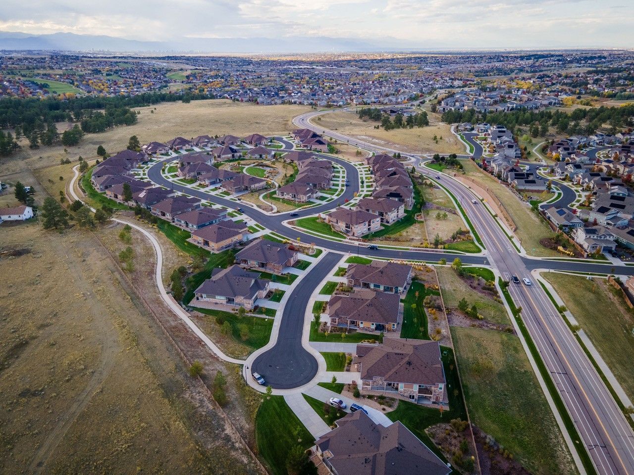 Aerial view of a suburban neighborhood with curving streets, houses, and open fields beside a road and rail line.