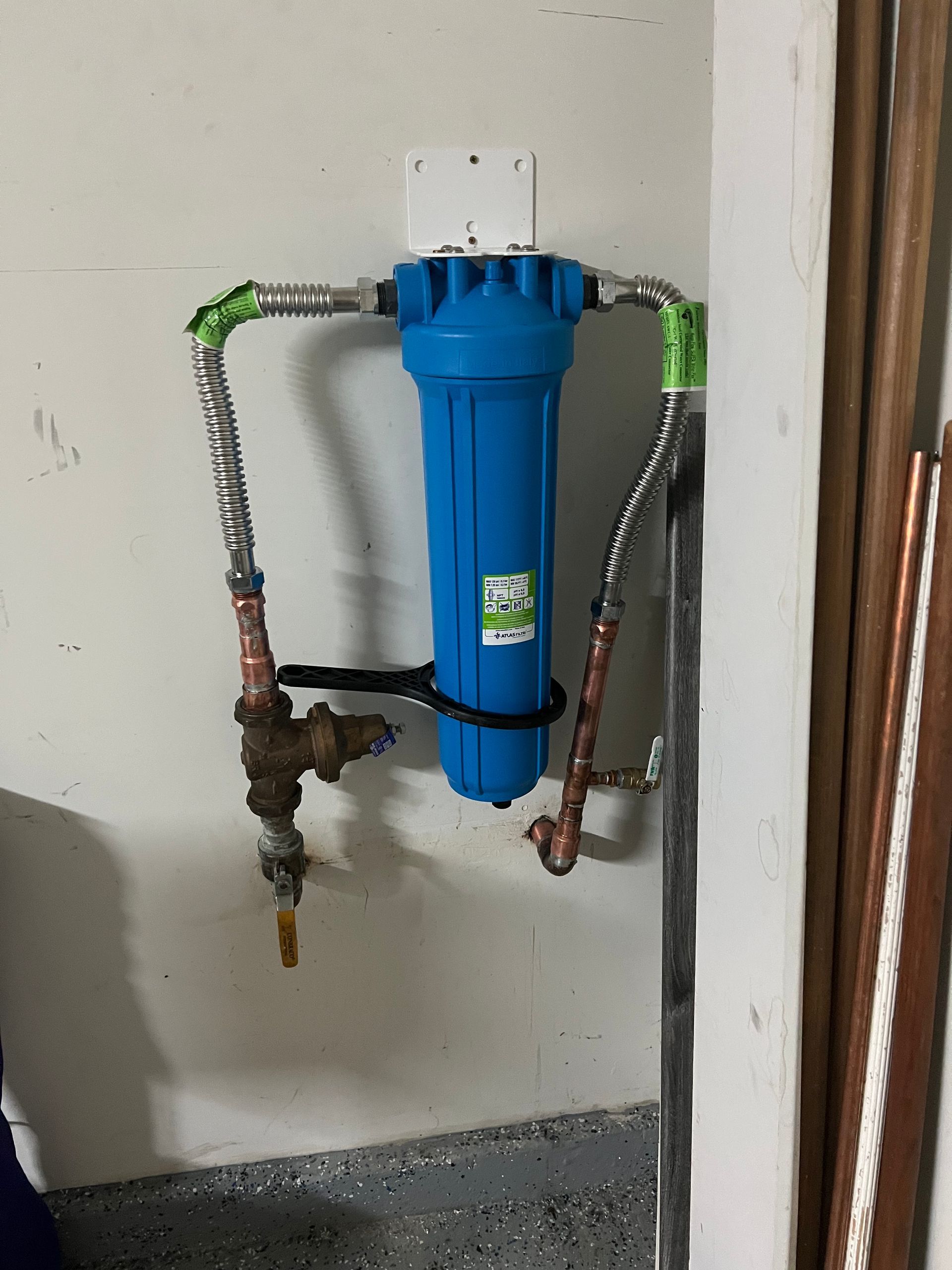 A blue water filter is attached to a pipe on a wall.