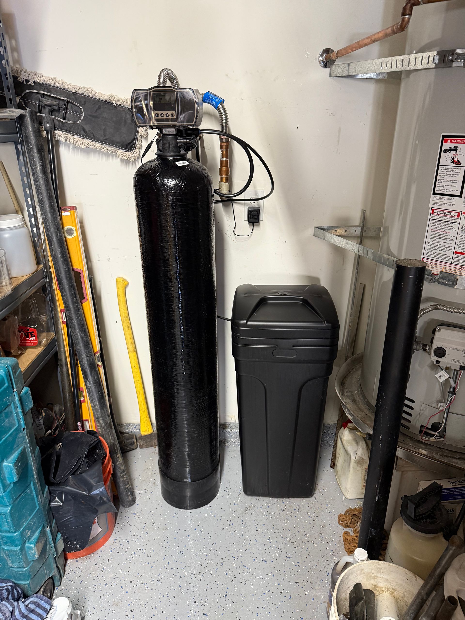 A water filter is sitting in a garage next to a trash can.