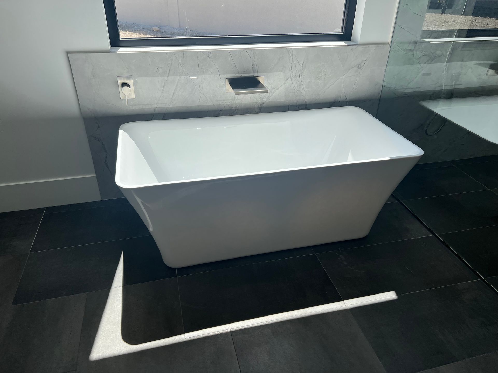 A white bathtub in a bathroom next to a window