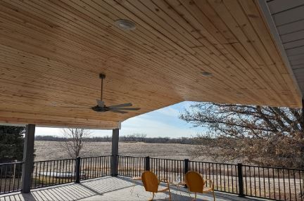 A wooden porch with a ceiling fan and chairs.