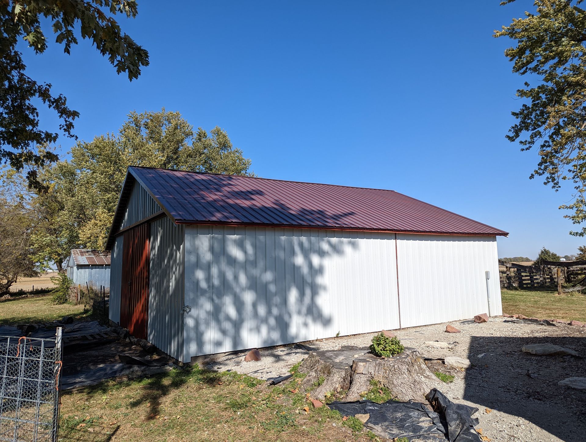 A white barn with a red roof is sitting in the middle of a grassy field.