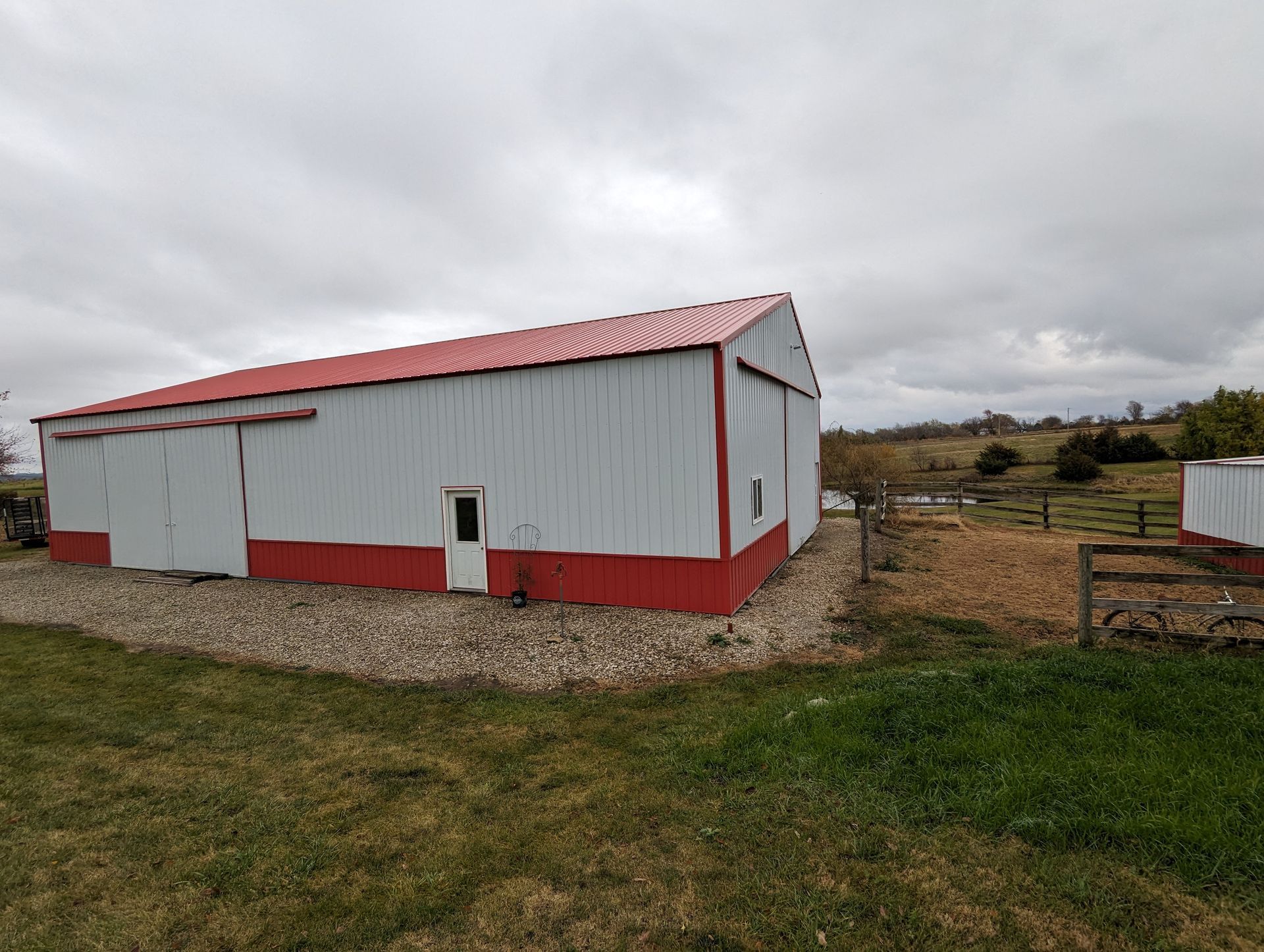 A white barn with a red roof is sitting in the middle of a grassy field.