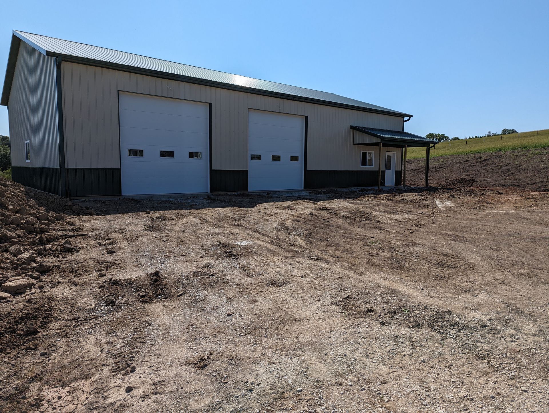 A large building with two garage doors is sitting in the middle of a dirt field