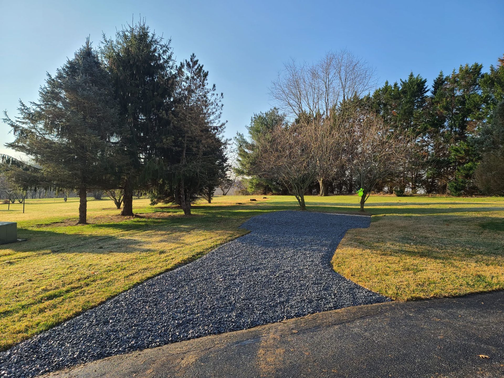 A gravel driveway leading to a grassy field with trees on both sides.