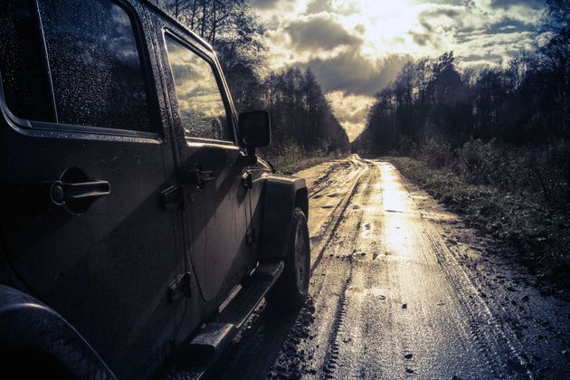 Black jeep on a wet muddy road at sunset, with sunlight reflecting through trees.