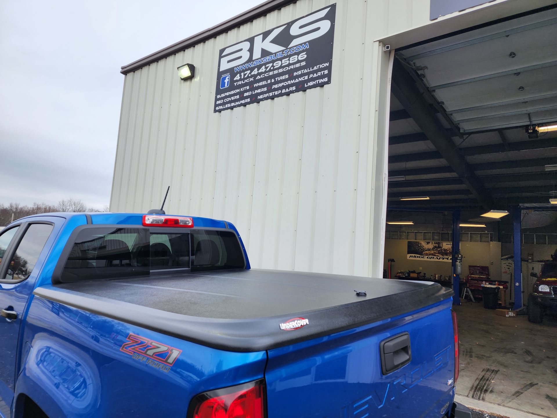 Blue pickup truck parked outside a BKS auto shop with an open garage bay