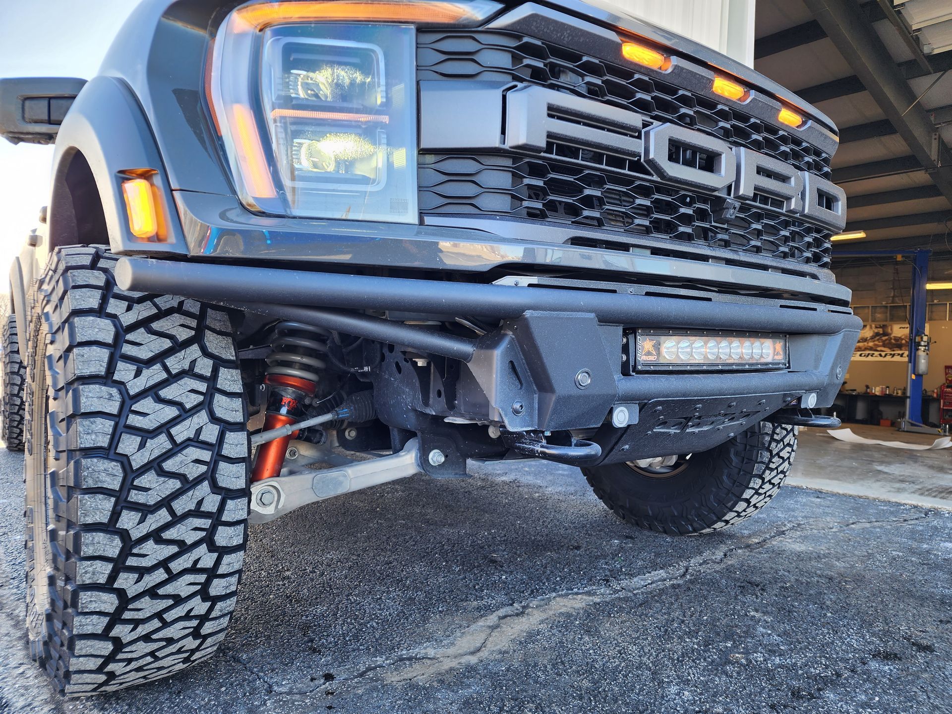 Lifted black Ford truck with off-road tires parked indoors, front view