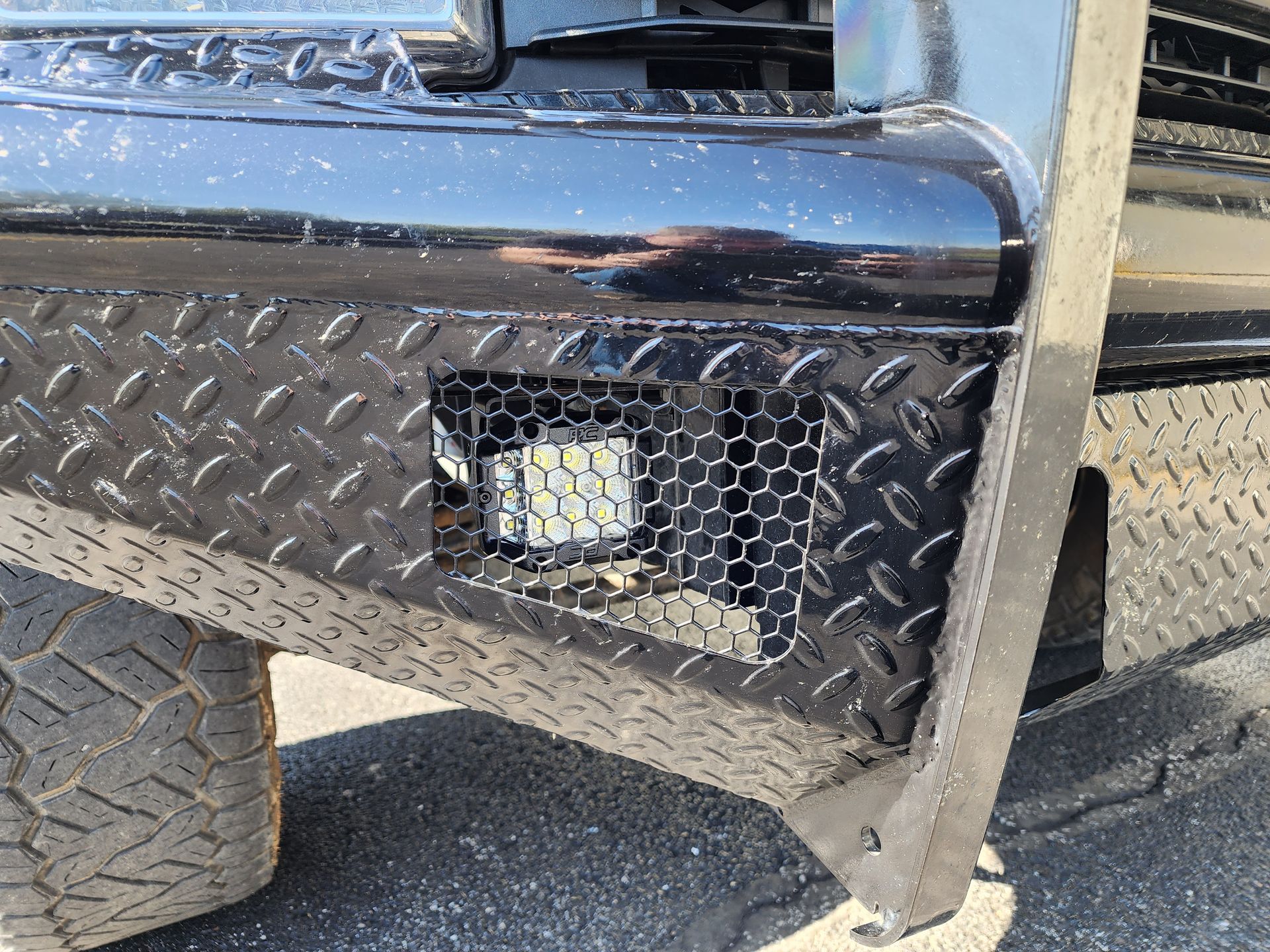 Close-up of a black pickup truck bumper with diamond-plate panel and a small light.