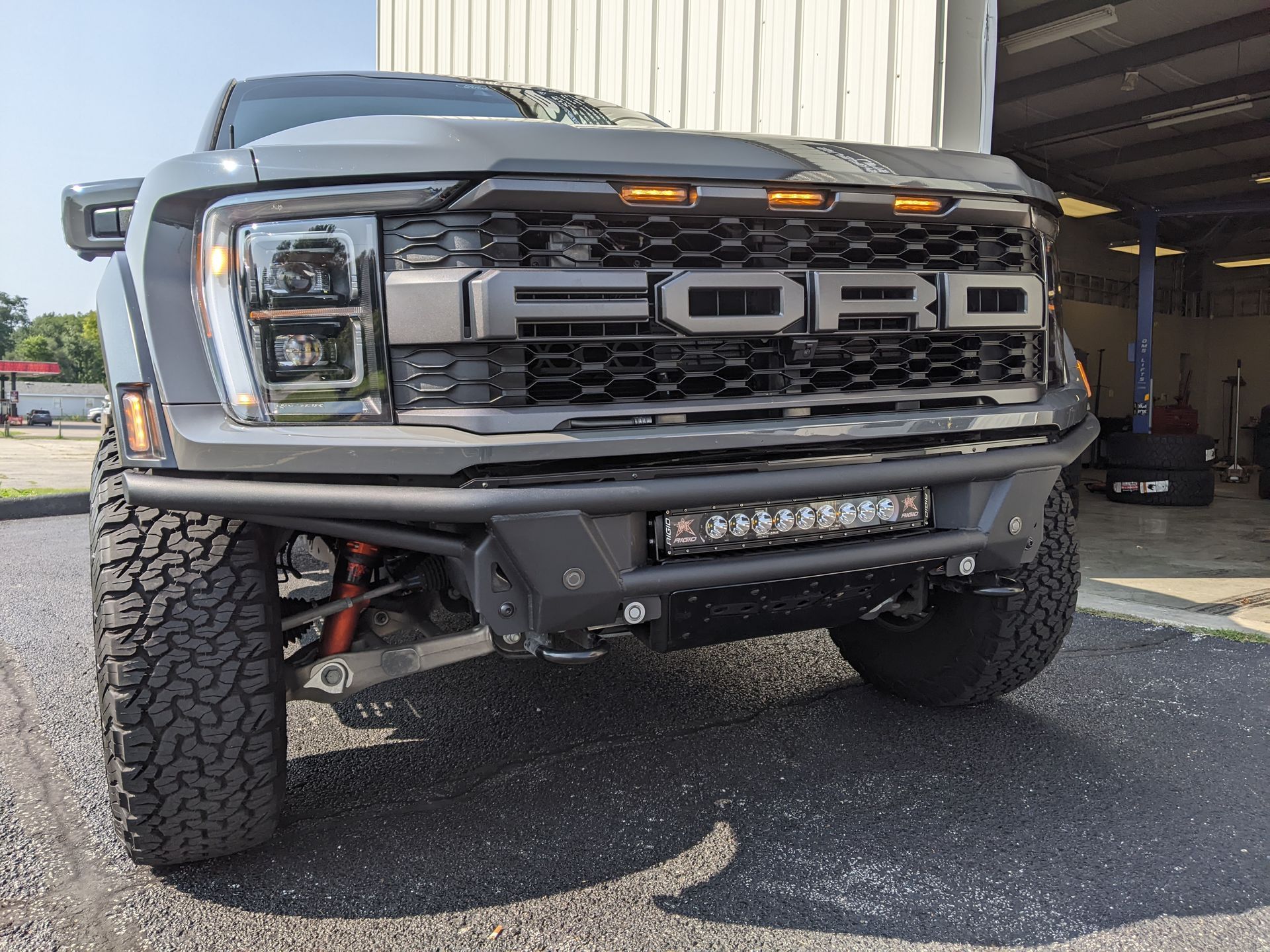 Front view of a lifted black Ford truck with off-road tires parked outside a metal building.