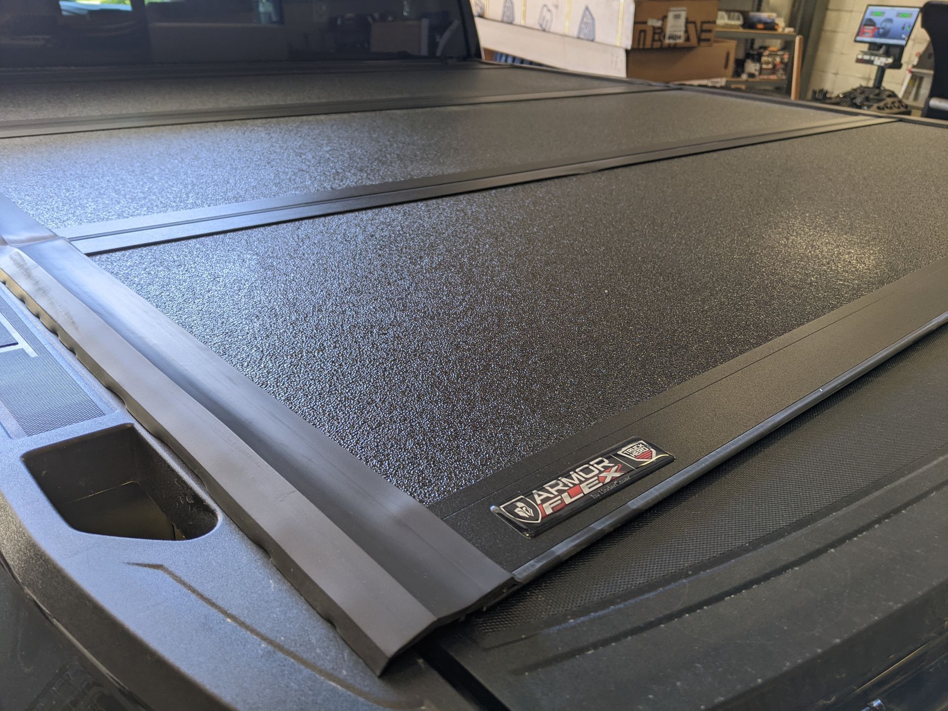 Textured black tri-fold truck bed cover installed on a pickup in a garage