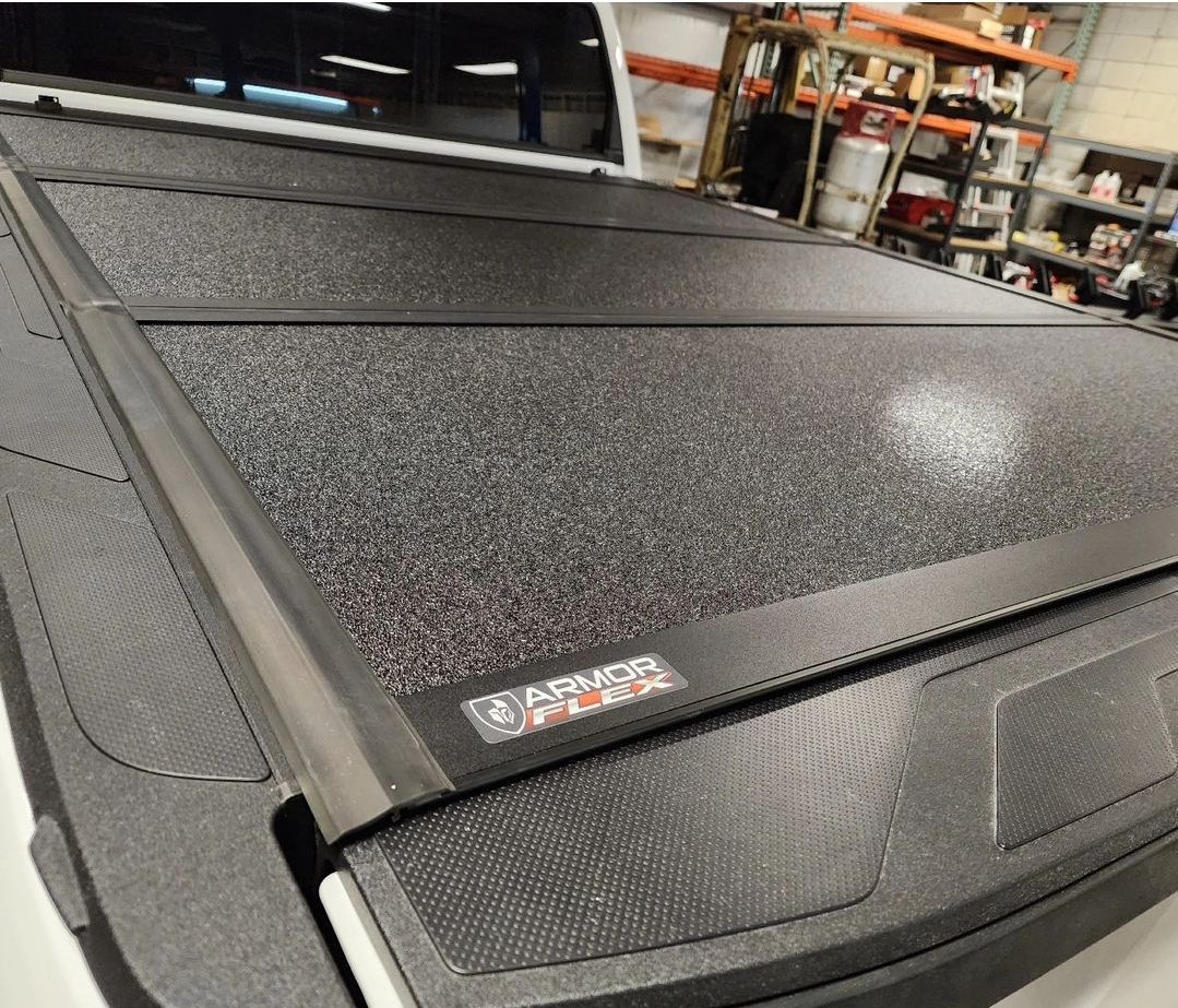 Black textured truck bed cover in a warehouse, with a small label on the edge.