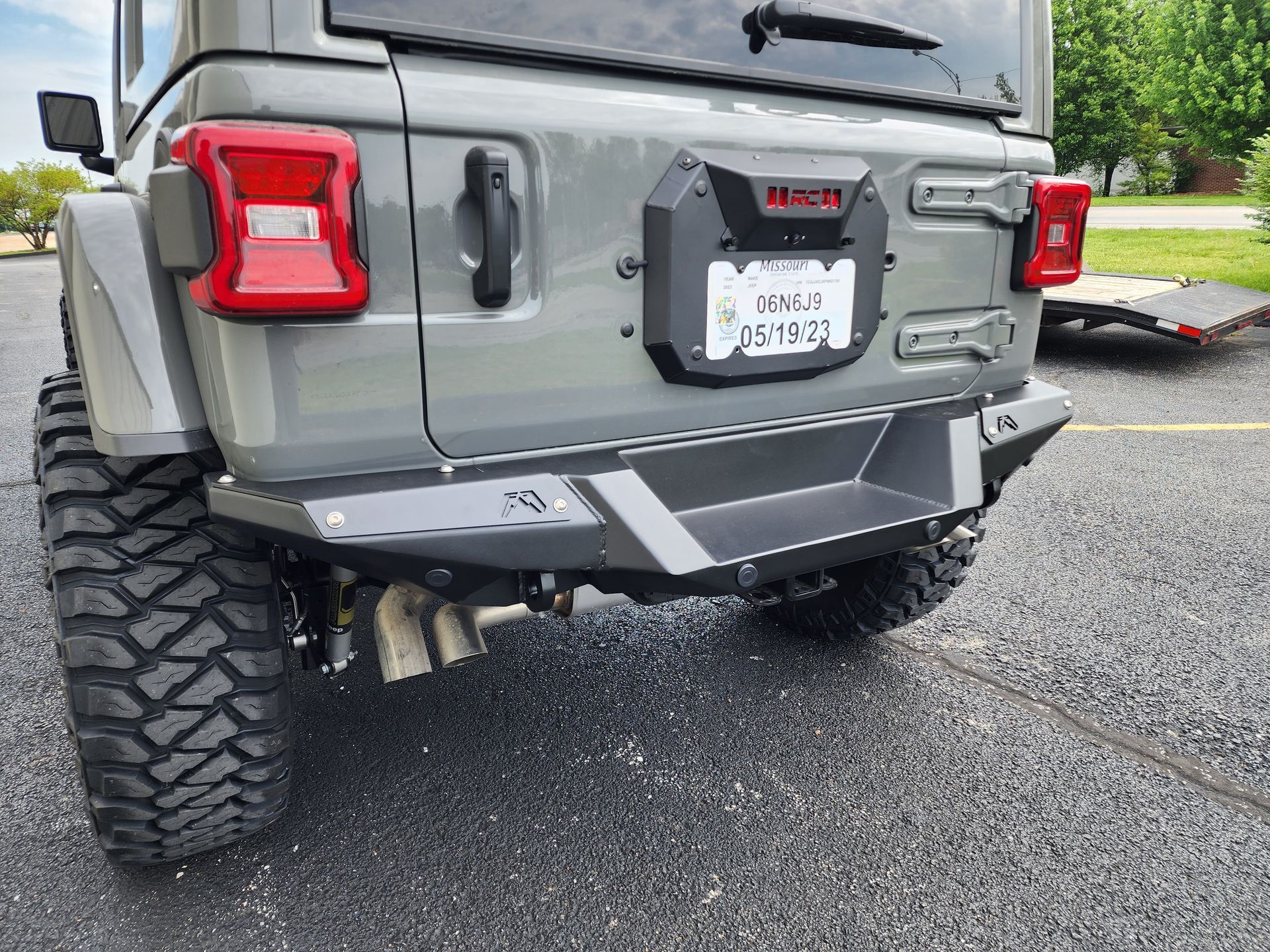 Grey off-road Jeep rear view with lifted suspension and oversized tires in a driveway