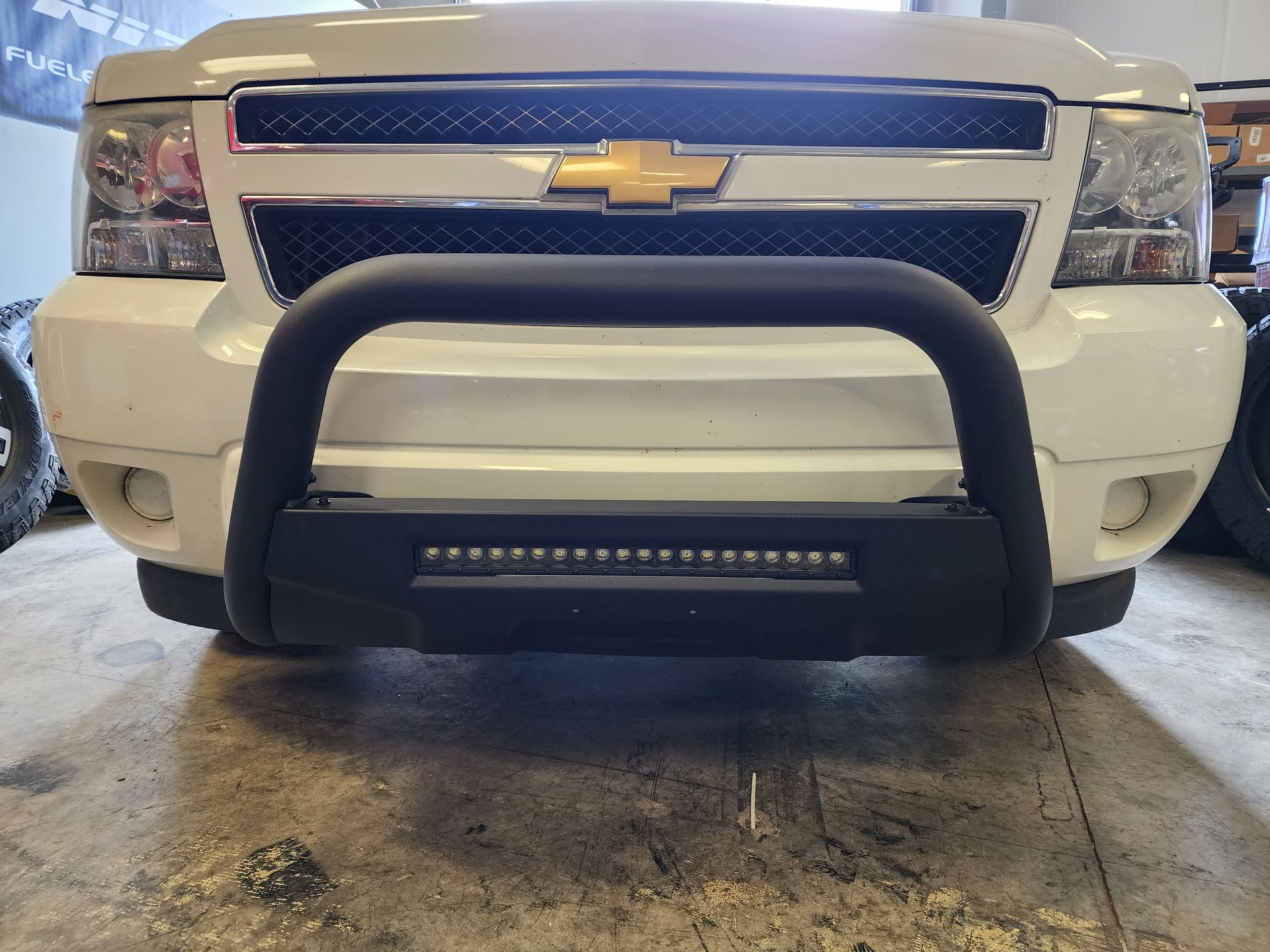 Front view of a white Chevrolet truck with a black grille guard parked in a garage.