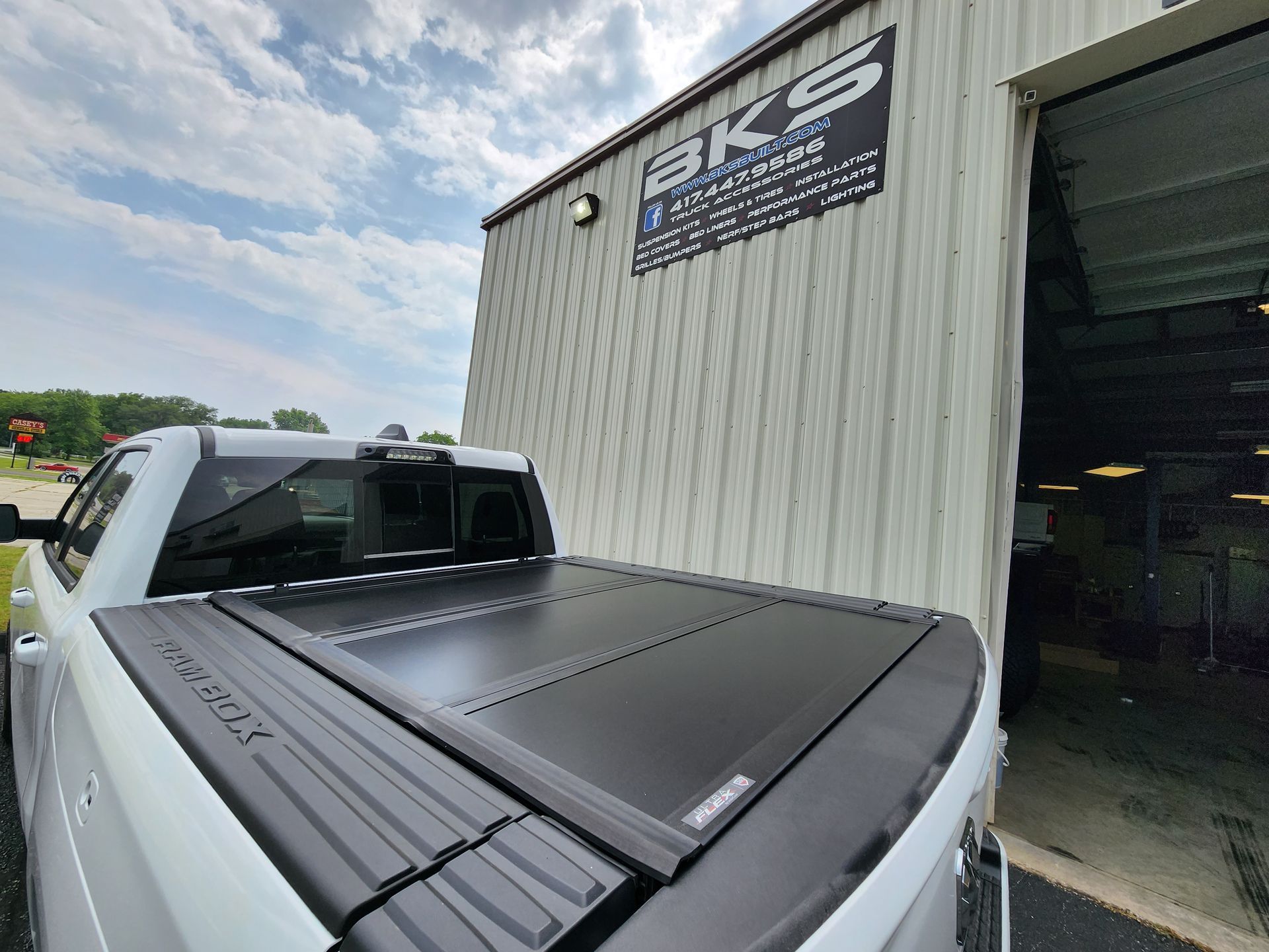 White truck with a black tonneau cover parked beside an open garage door at an auto shop.
