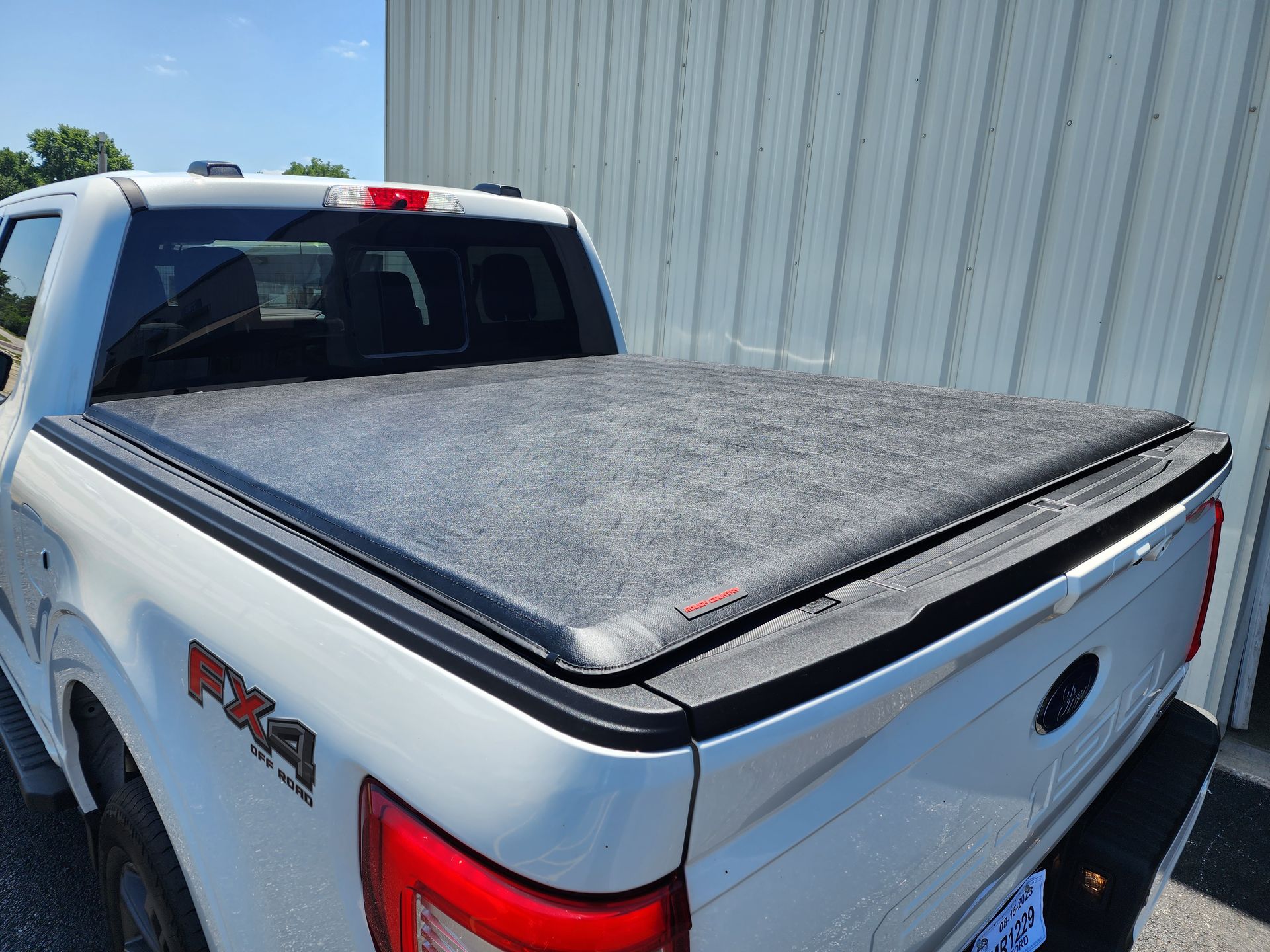 White pickup truck with a covered bed parked beside a metal building in bright sunlight