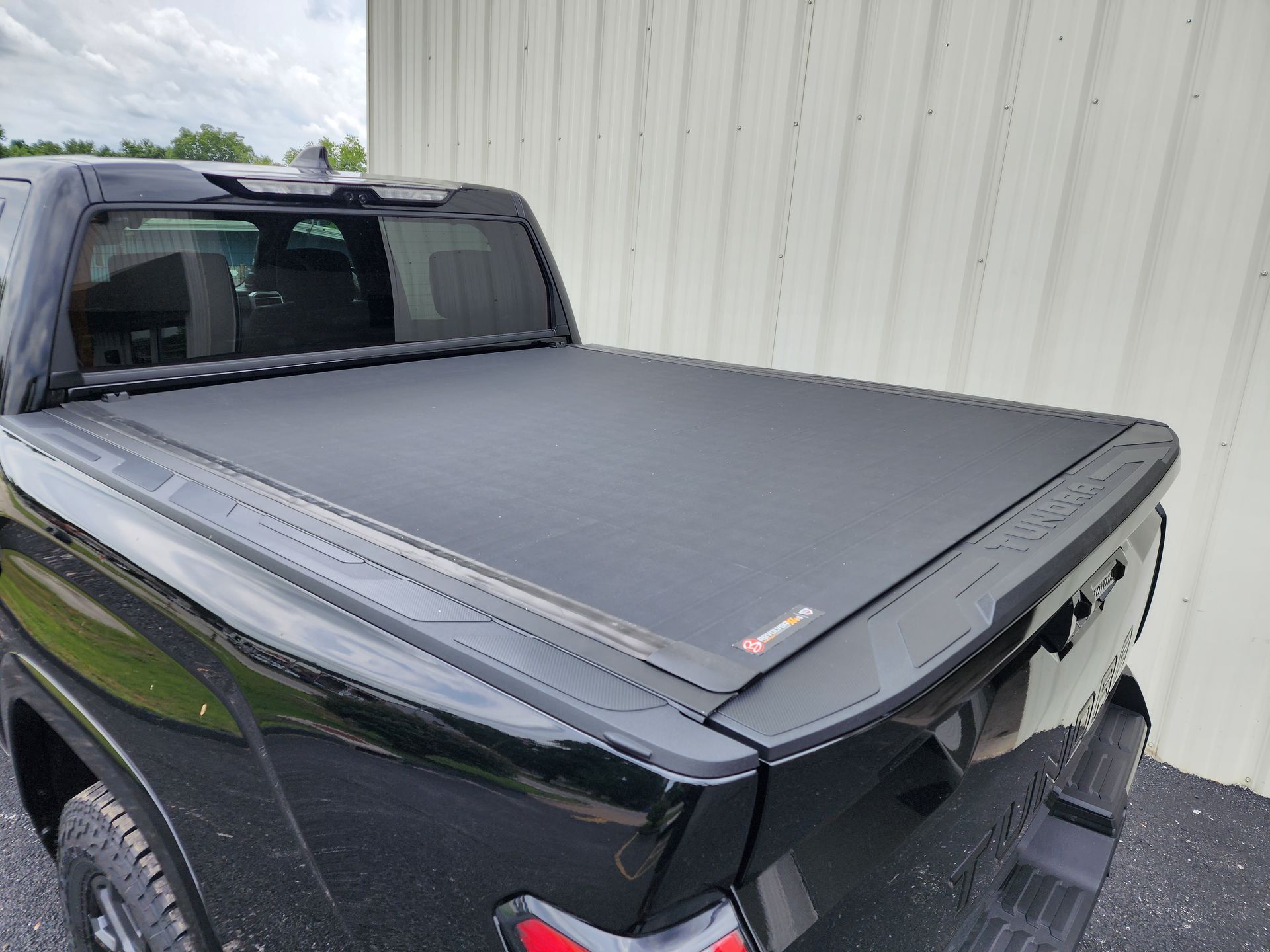 Black pickup truck with a gray tonneau cover parked beside a metal building
