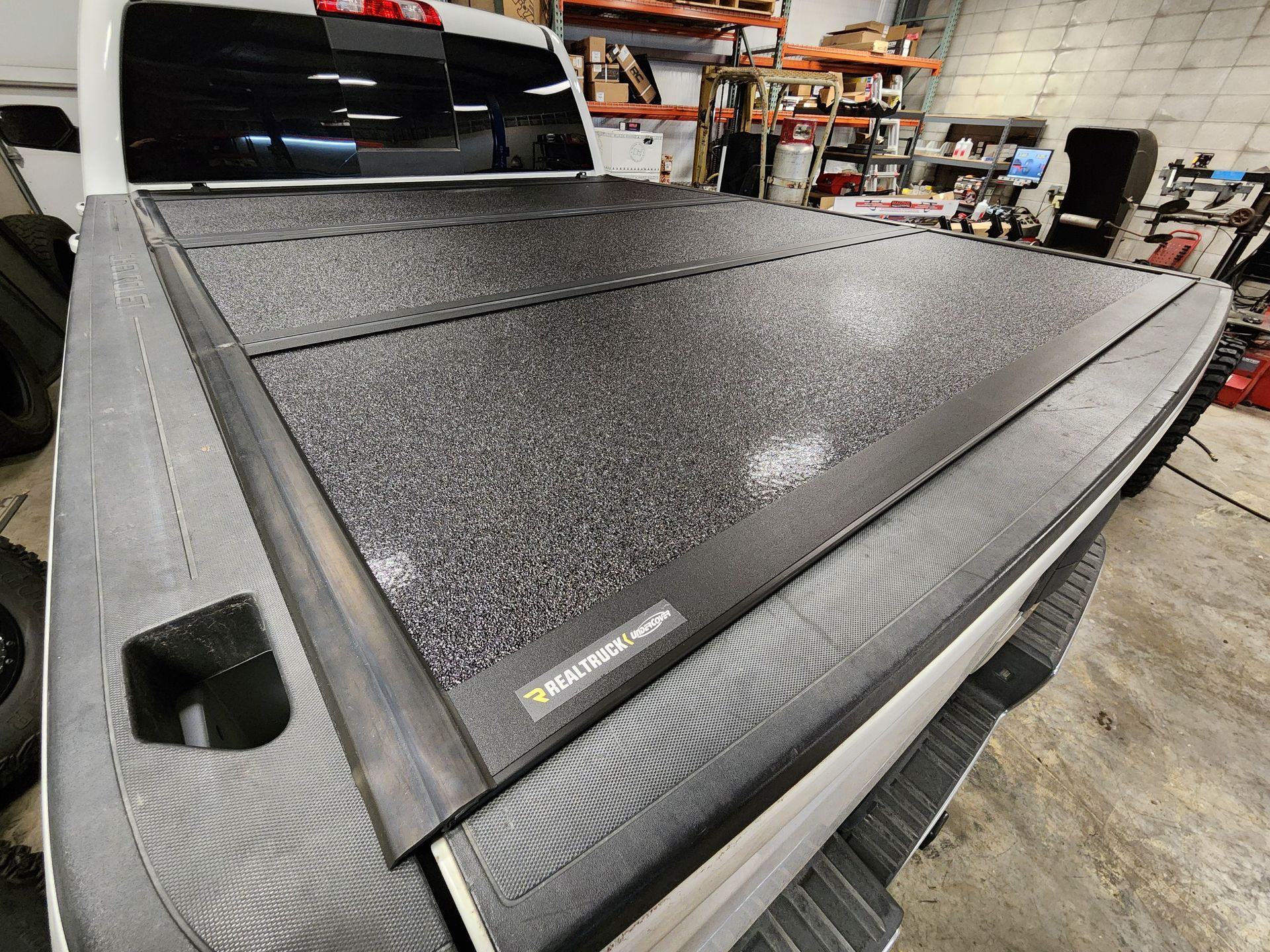 Black textured truck bed cover in a workshop, shown close-up on a pickup bed
